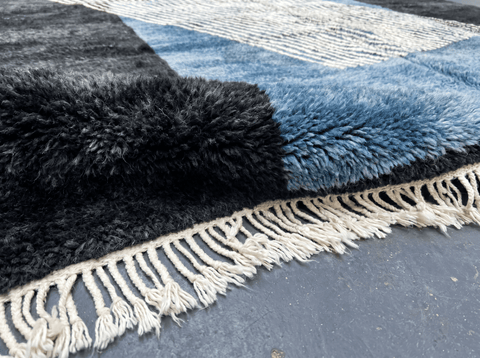 Detail view of the deep charcoal rug's edge, featuring fringe detail and layered texture.