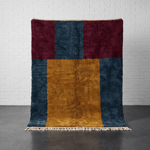 Front view of a handmade Moroccan rug featuring a geometric pattern in burgundy, teal, and gold with fringe edges.