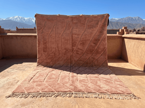 Lifestyle shot of a dusty rose Moroccan rug featuring pink and brown colors with a textured surface.