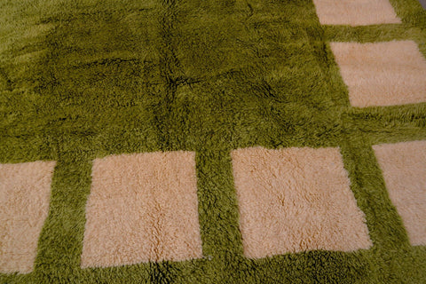 Close-up detail of the olive green Moroccan rug featuring its geometric design and fringe edges.