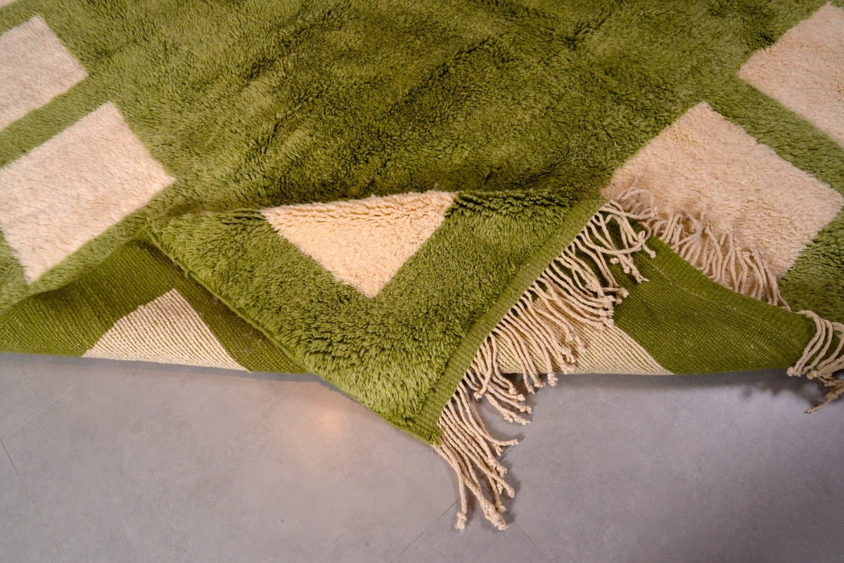 Close-up detail of the olive green Moroccan rug showing its geometric pattern and fringe edges.