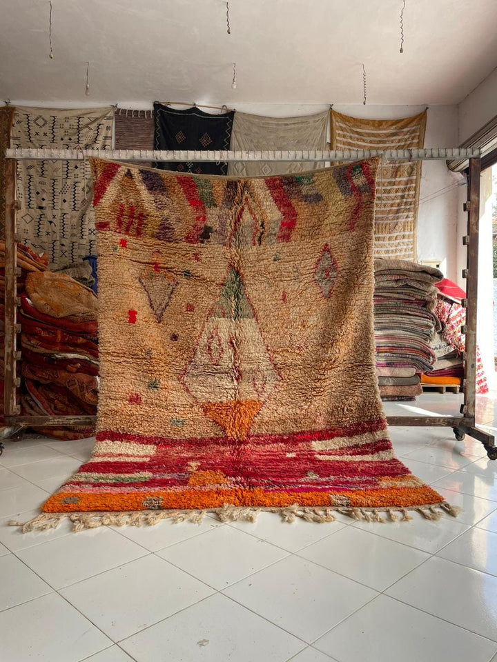 Lifestyle shot of a vintage Moroccan rug featuring red and orange colors with fringe edges.