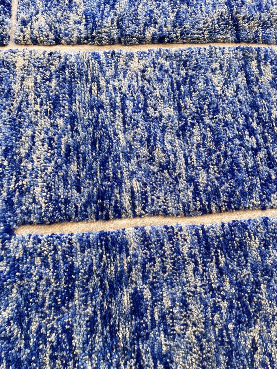 Detail shot of a blue wool rug with a thick pile and woven design.