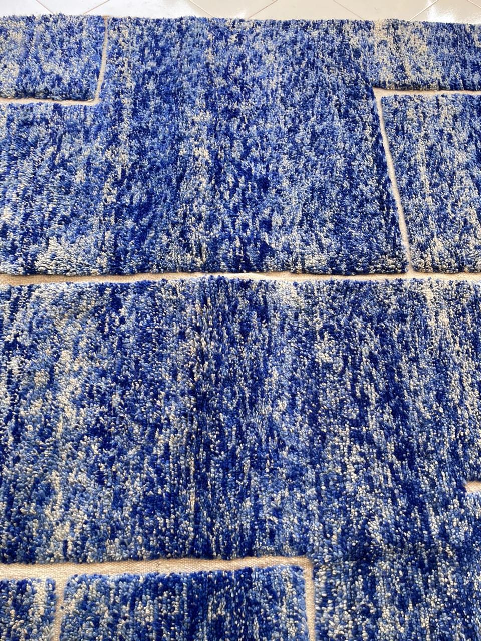 Detail view of a blue wool rug featuring a textured surface and geometric design.