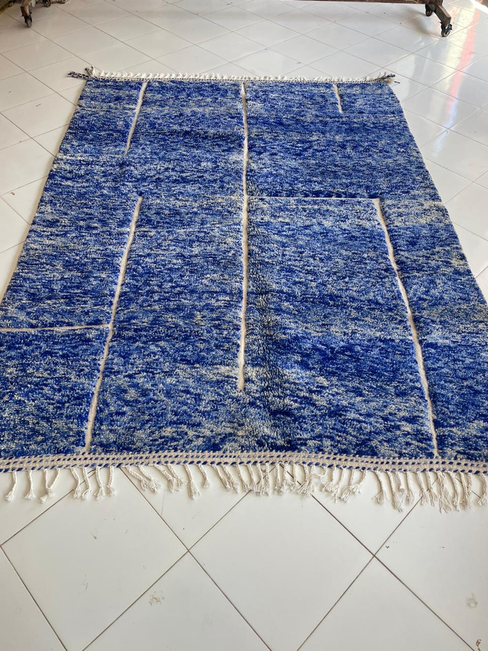 Other angle of a blue wool rug with a geometric pattern and fringed edges.