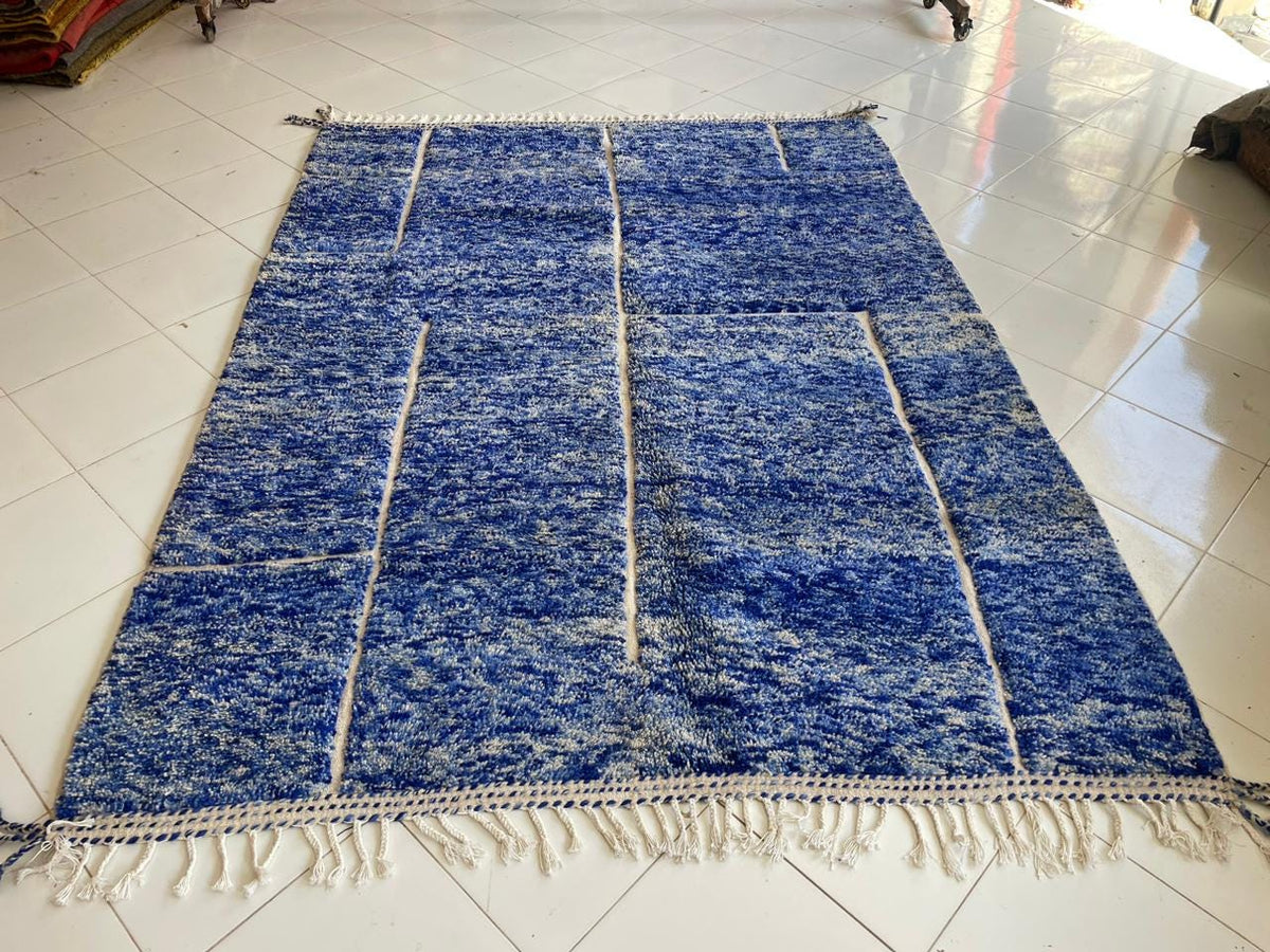 Top view of a blue Moroccan rug featuring fringed edges against a natural backdrop.