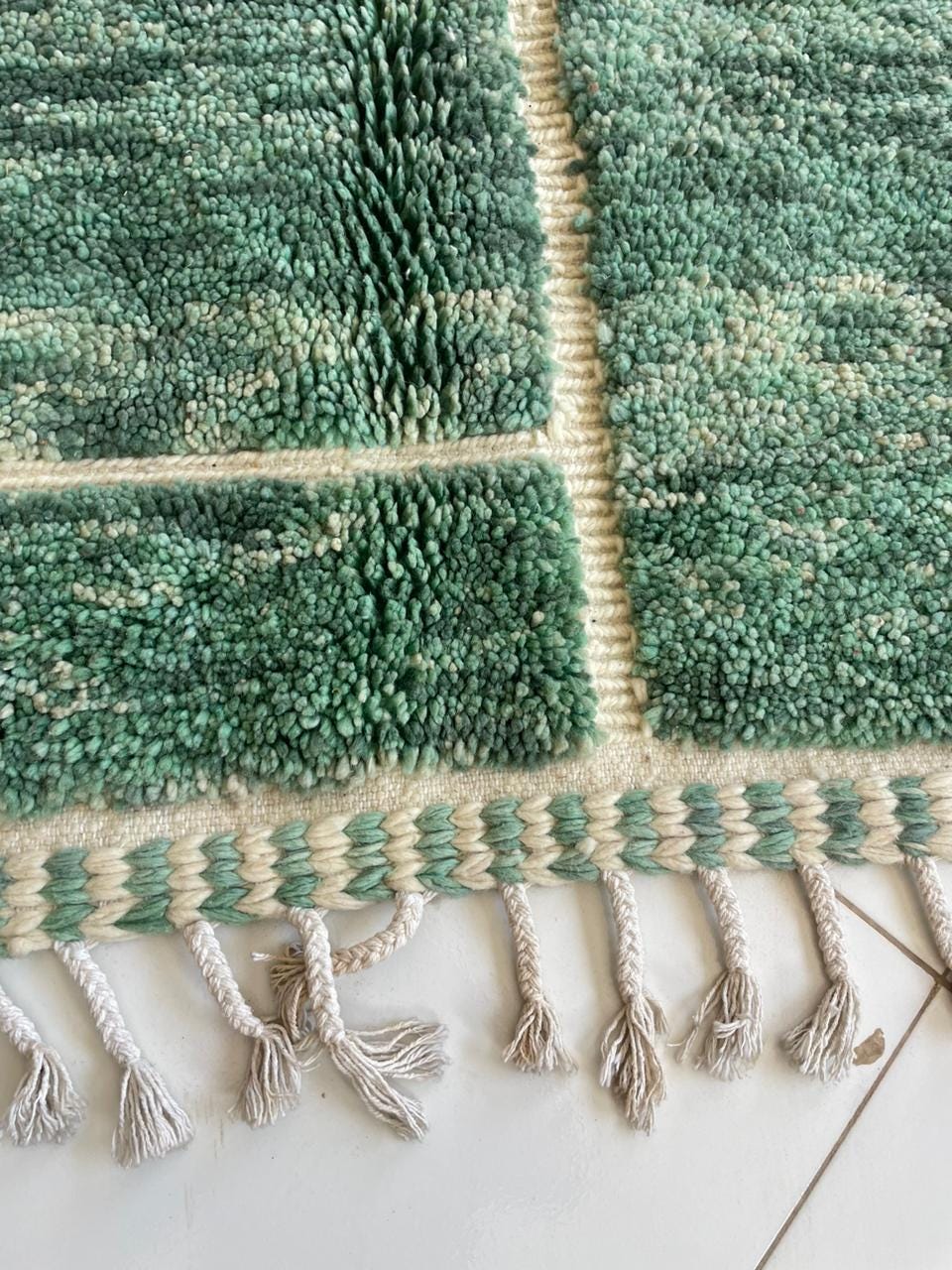 Detail view of the green vintage Beni Ourain Moroccan rug featuring fringe edges in a natural background.