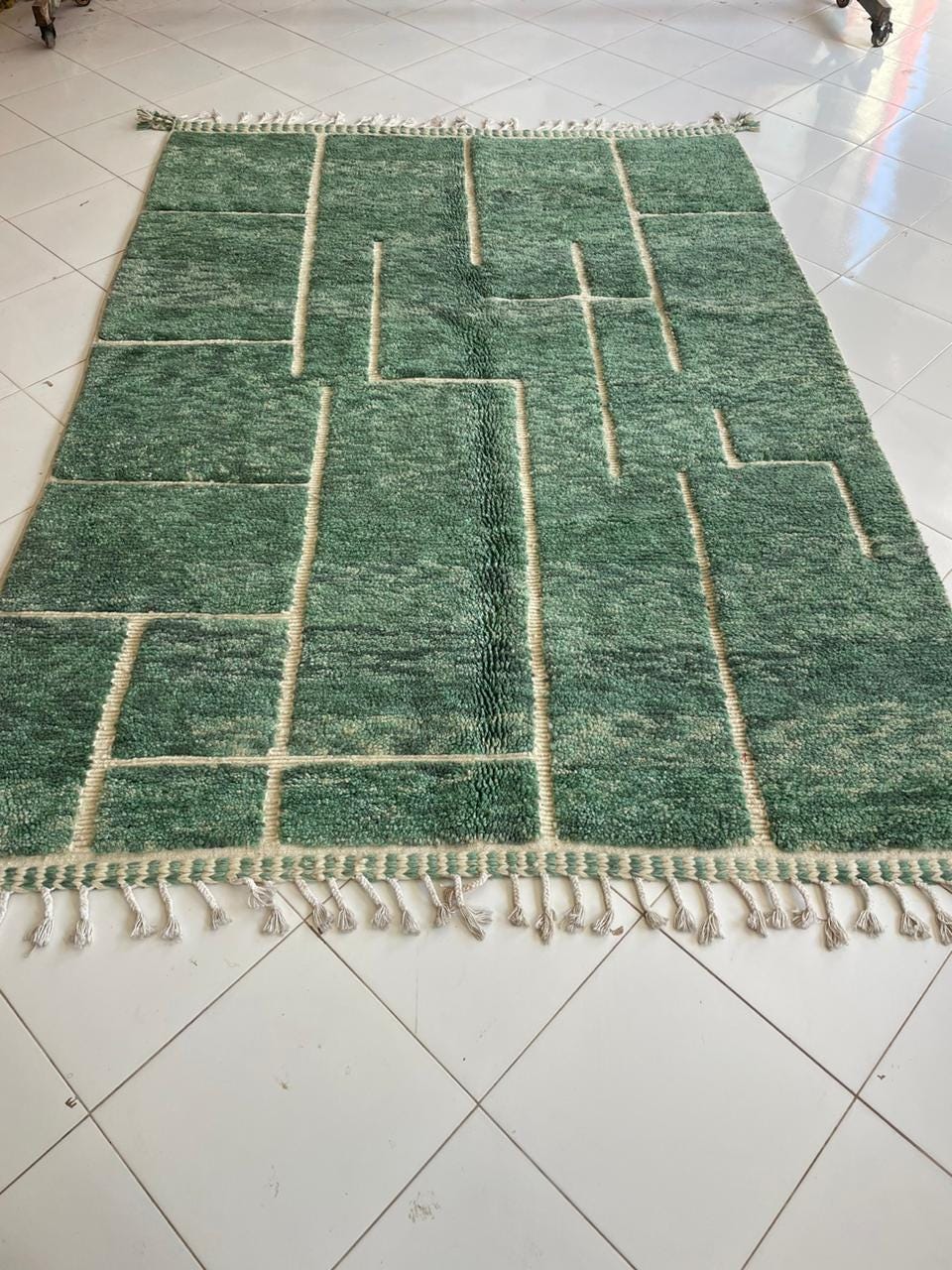 Lifestyle shot of a green vintage Beni Ourain Moroccan rug with geometric design and fringed edges in a natural setting.