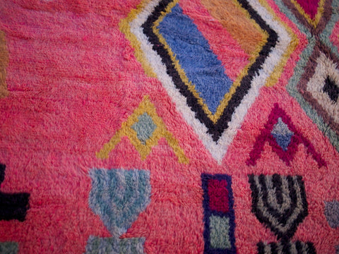 Close-up of a pink Moroccan rug displaying geometric shapes against a natural backdrop.