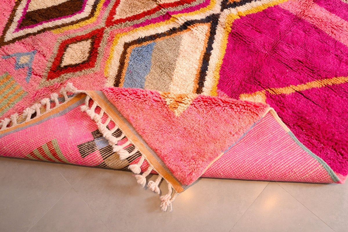 Detail close-up of a pink Moroccan rug showcasing abstract designs and fringe in a studio setting.