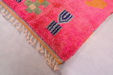 Detail close-up of a pink Moroccan rug featuring fringe and geometric patterns in a studio setting.