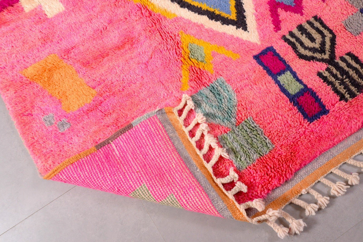 Detail close-up of a pink Moroccan rug with colorful patterns and fringe in a studio setting.