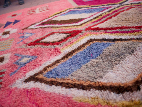 Detail view of a pink Moroccan rug featuring textured surface and colorful motifs.