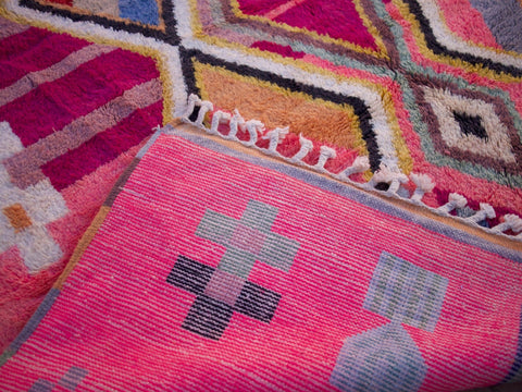 Close-up of a pink Moroccan rug featuring geometric patterns and soft shag in a natural setting.