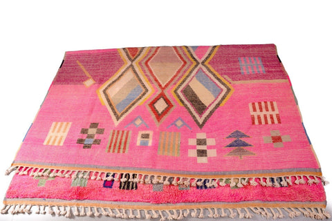 Top view of a pink Moroccan rug displaying geometric patterns against a white background.