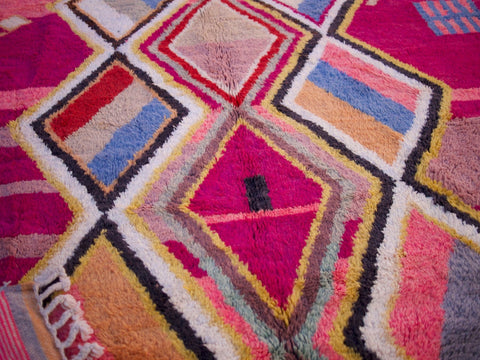 Detail shot of a pink Moroccan rug with geometric patterns in a natural background.