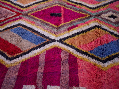 Detail view of a pink Moroccan rug featuring colorful patterns in a natural background.