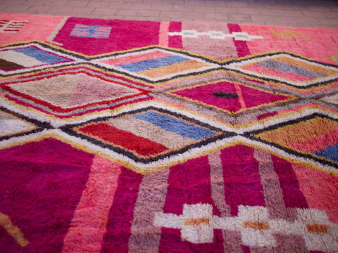 Close-up of a pink Moroccan rug with diamond patterns in a natural setting.
