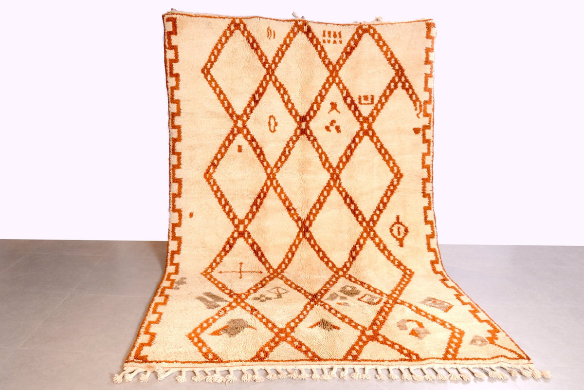 Lifestyle shot of a diamond pattern rug in cream and orange with fringed edges.