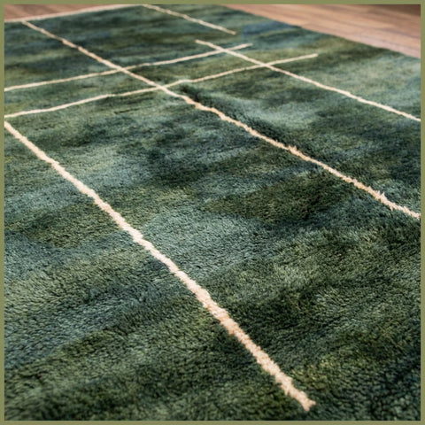 Side view of a green Moroccan rug with a thick pile and fringe edges.