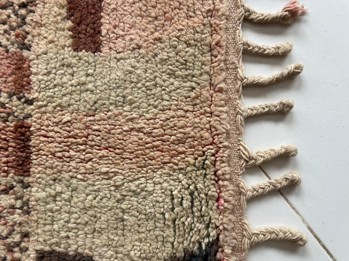 Close-up detail of a vintage Moroccan rug featuring fringe edges and a textured surface in beige and brown.