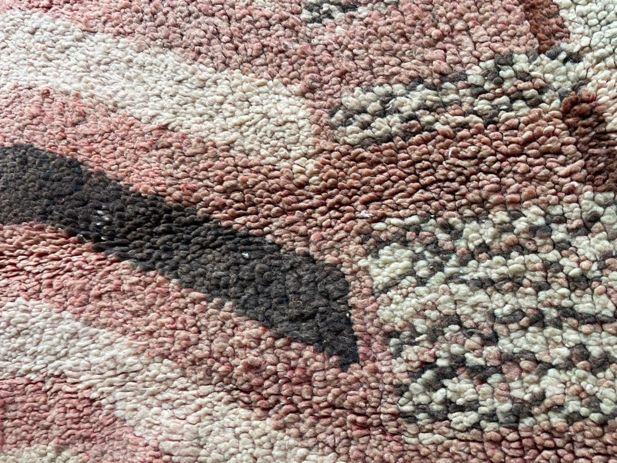 Close-up detail of tribal patterns on a vintage Moroccan rug featuring a faded design in red, black, and cream.