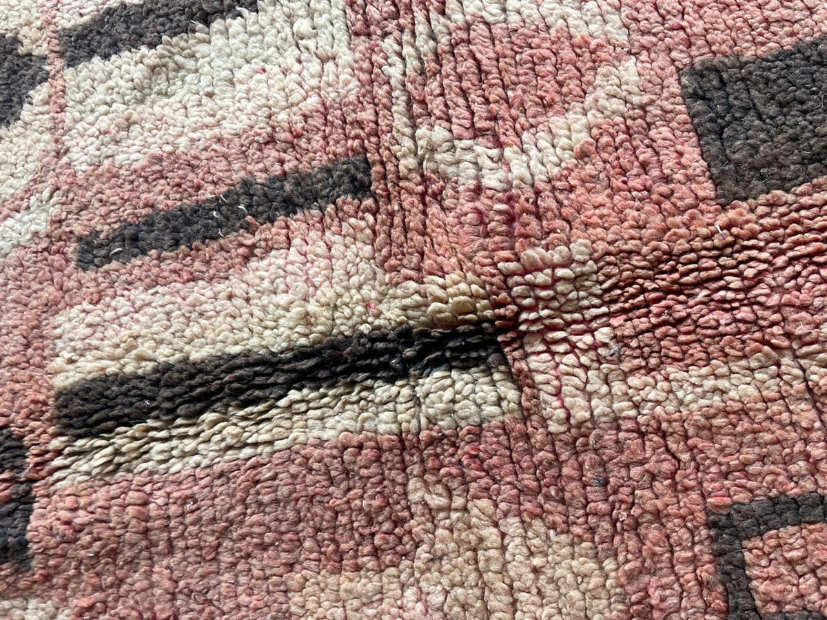 Close-up detail of tribal patterns on a vintage Moroccan rug with a faded design in red, black, and cream.