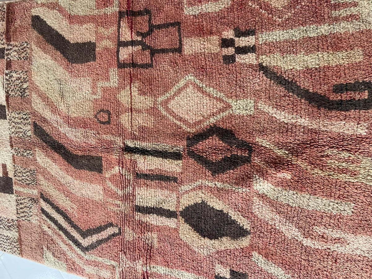 Close-up detail of tribal patterns on a vintage Moroccan rug with a faded design in red, black, and cream.