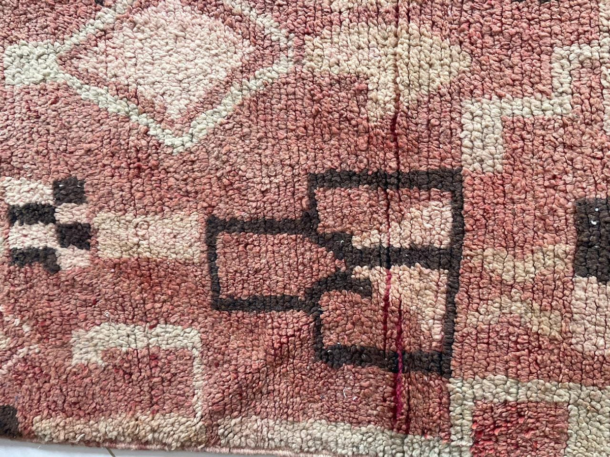 Close-up detail of geometric shapes on a vintage Moroccan rug in brown, red, and black.