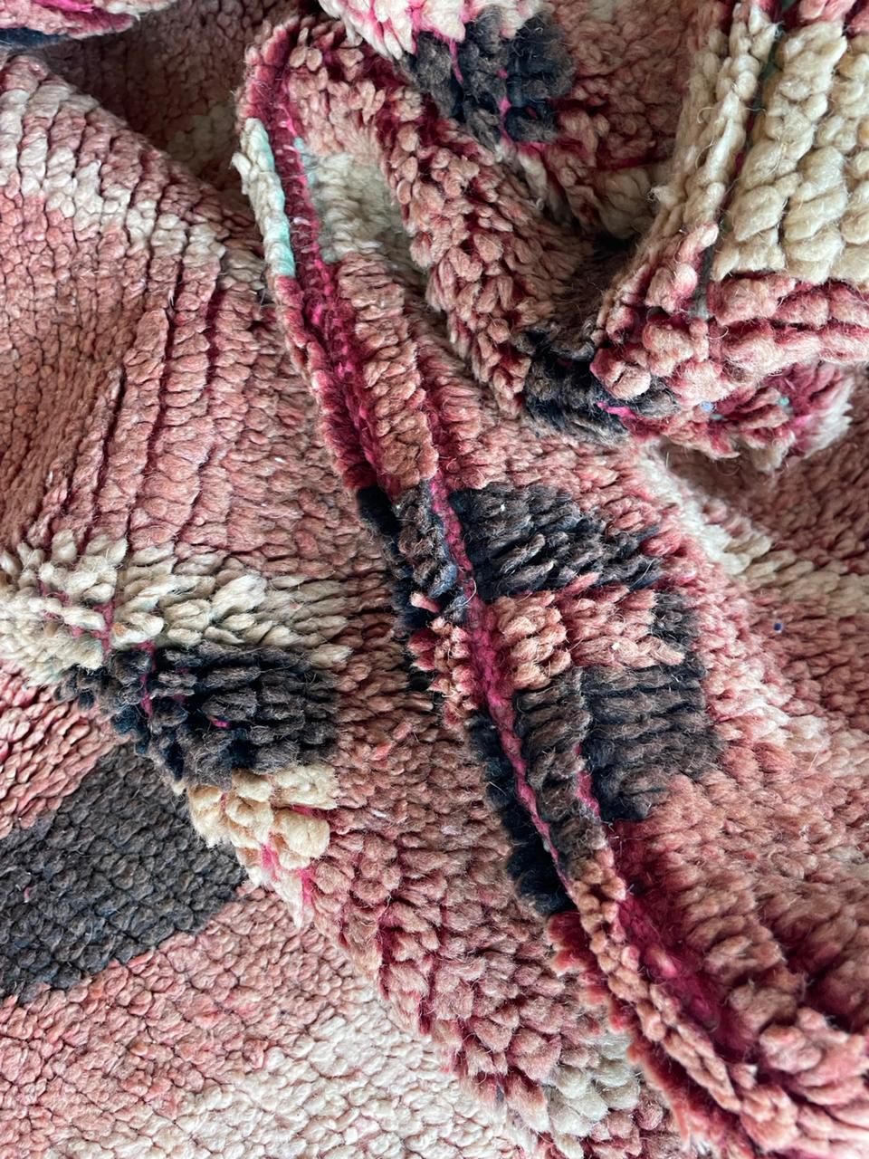 Close-up detail of tribal patterns on a vintage Moroccan rug with a faded design in red, beige, and black.
