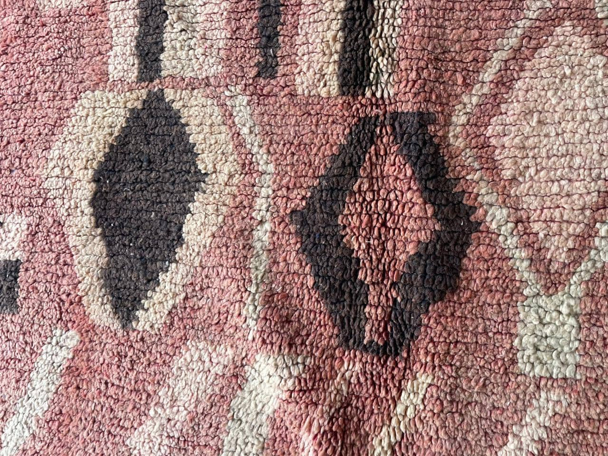 Close-up detail of tribal patterns on a vintage Moroccan rug with a faded design in red, black, and cream.