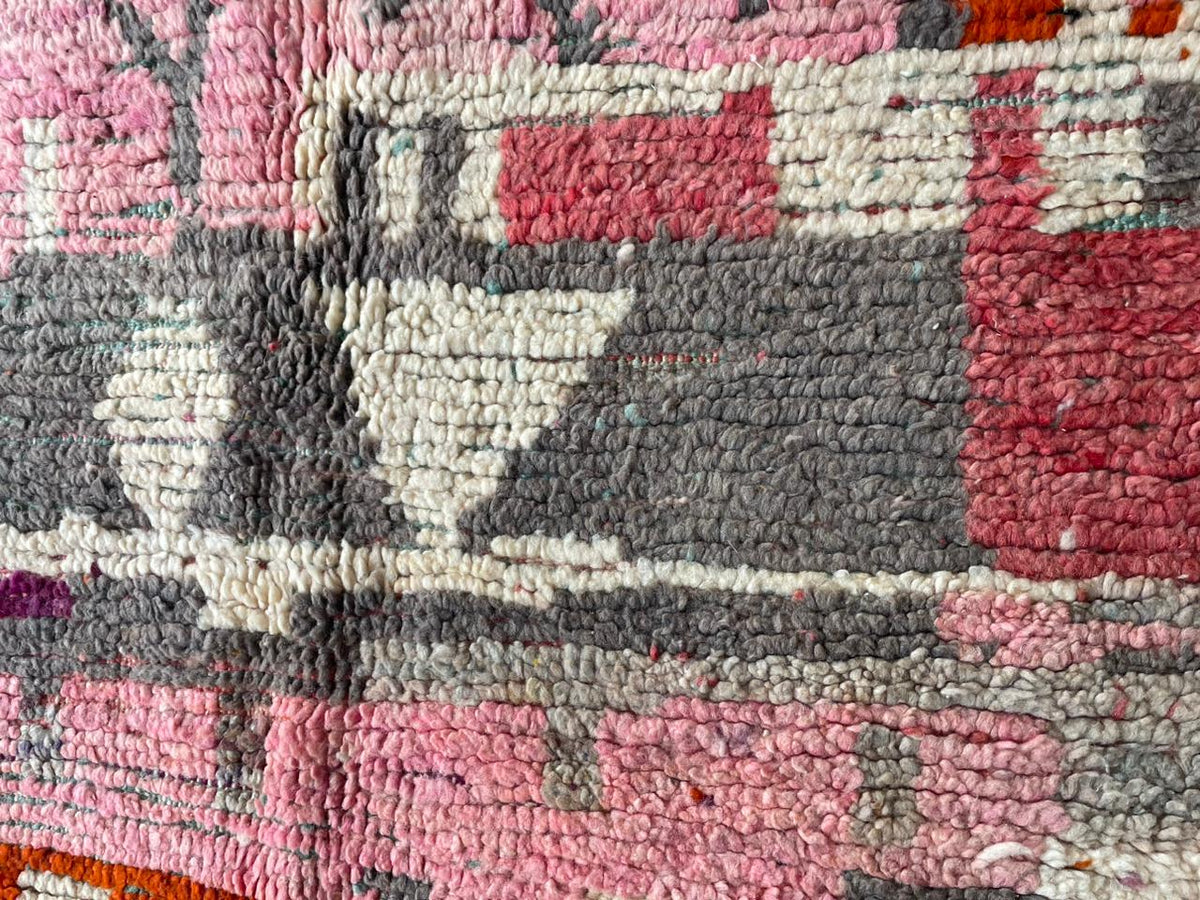 Close-up detail of a vintage Moroccan rug featuring tribal patterns and a faded design in red and gray.