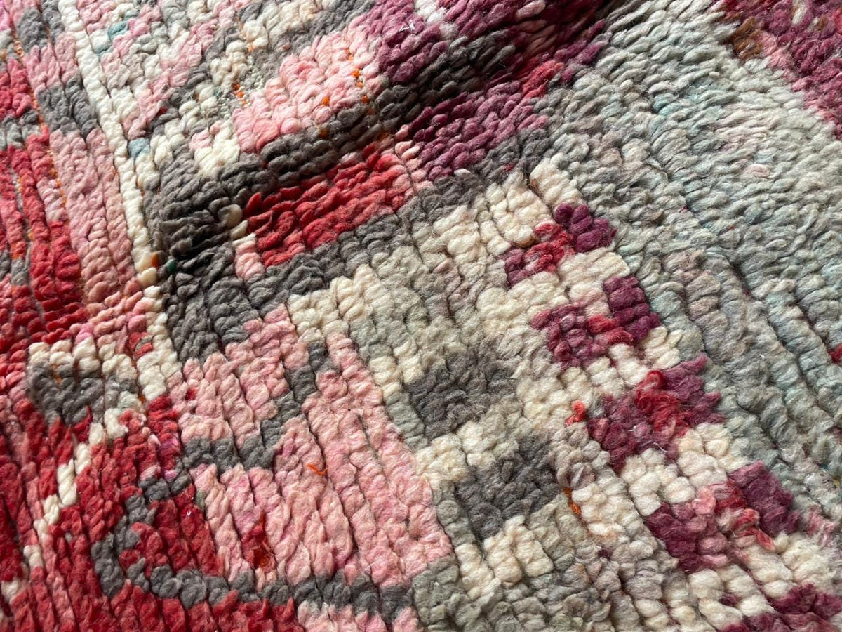 Close-up detail of a vintage Moroccan rug highlighting tribal patterns and fringe edges in red and gray.