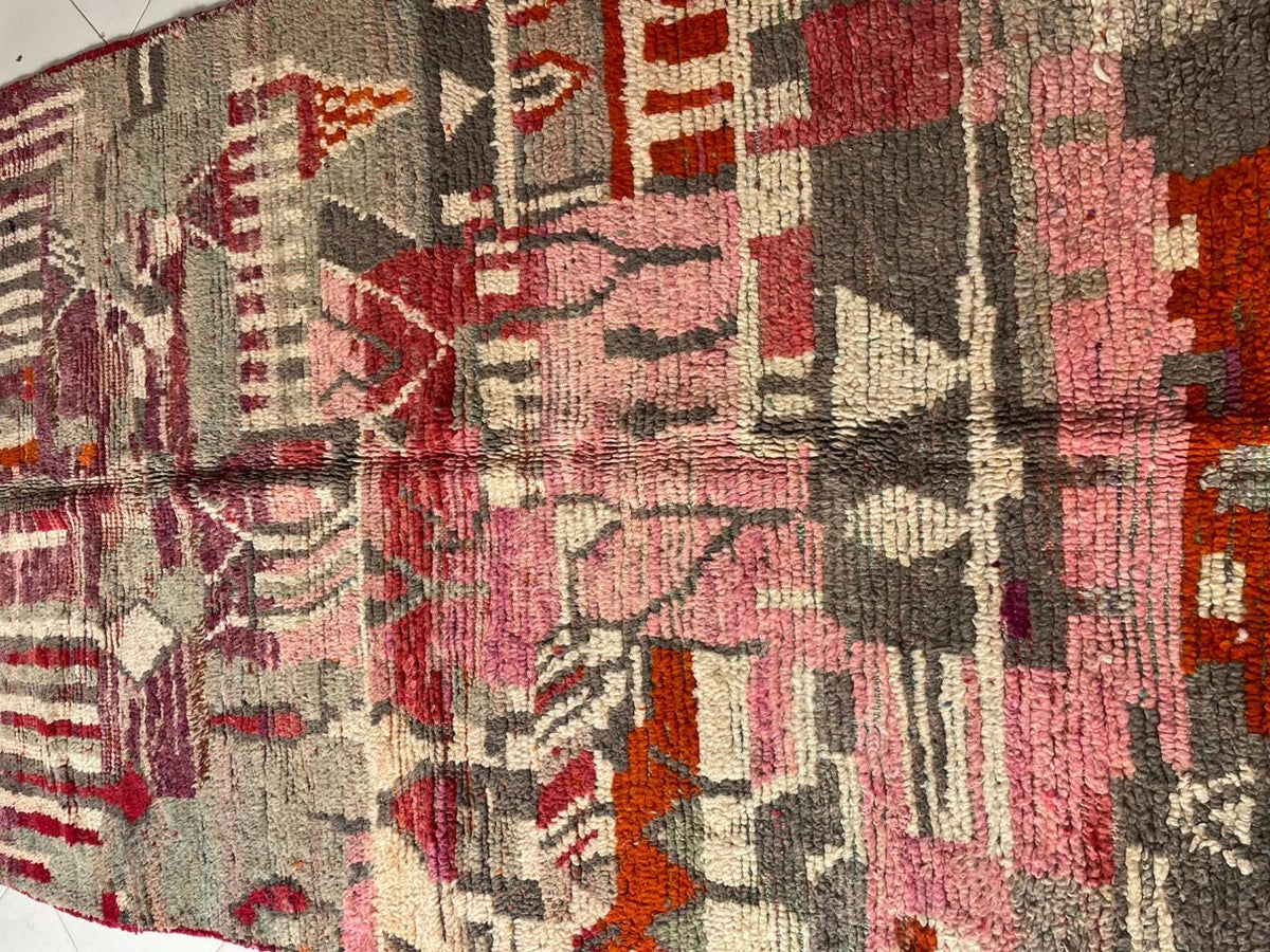 Close-up detail of a vintage Moroccan rug featuring tribal patterns and a faded design in red and gray.