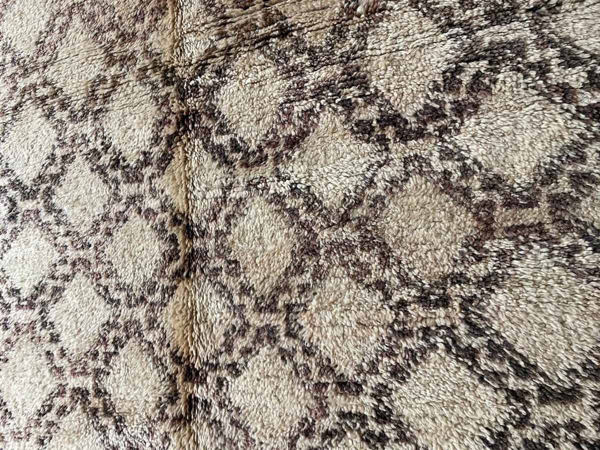 Detail shot of a vintage Moroccan rug featuring a diamond pattern in cream and brown.