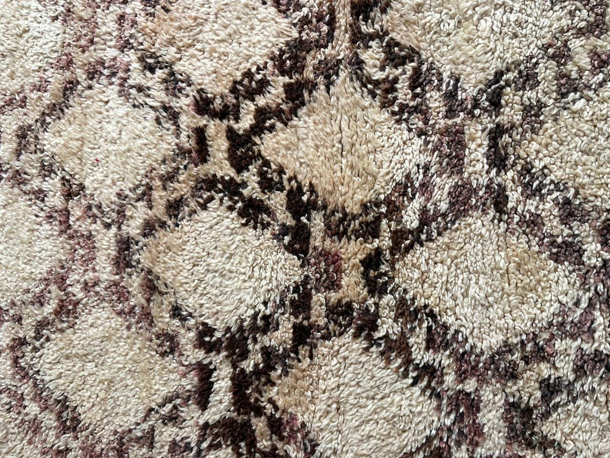 Detail shot of the geometric pattern and textured surface on a beige and brown Moroccan rug.