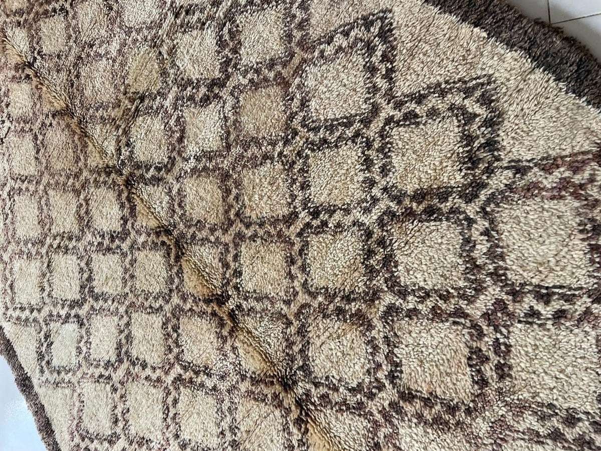 Close-up view of a vintage Moroccan rug with a geometric pattern in beige and brown.