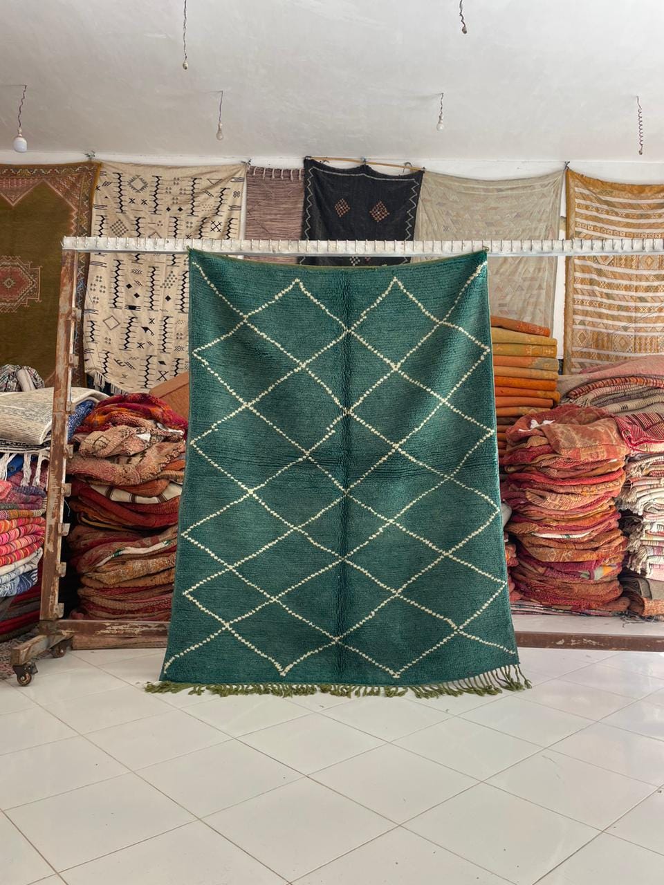 Lifestyle shot of a green Moroccan rug with a diamond pattern and fringe edges on a natural background.