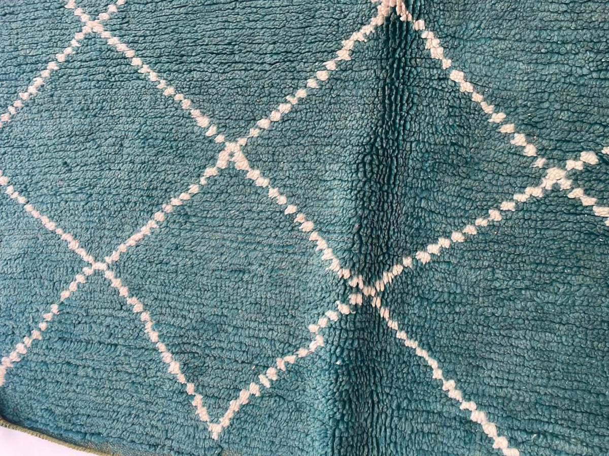 Detail close-up of a green turquoise rug with a diamond pattern and soft texture on a varied background.