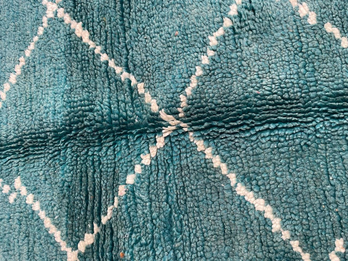 Detail close-up of a turquoise Moroccan rug showcasing a diamond pattern and soft texture on a white background.