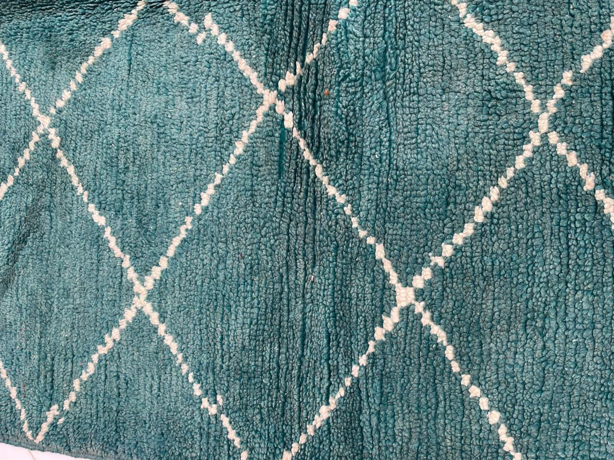Detail close-up of a green turquoise rug with a diamond design and soft fabric on a varied background.