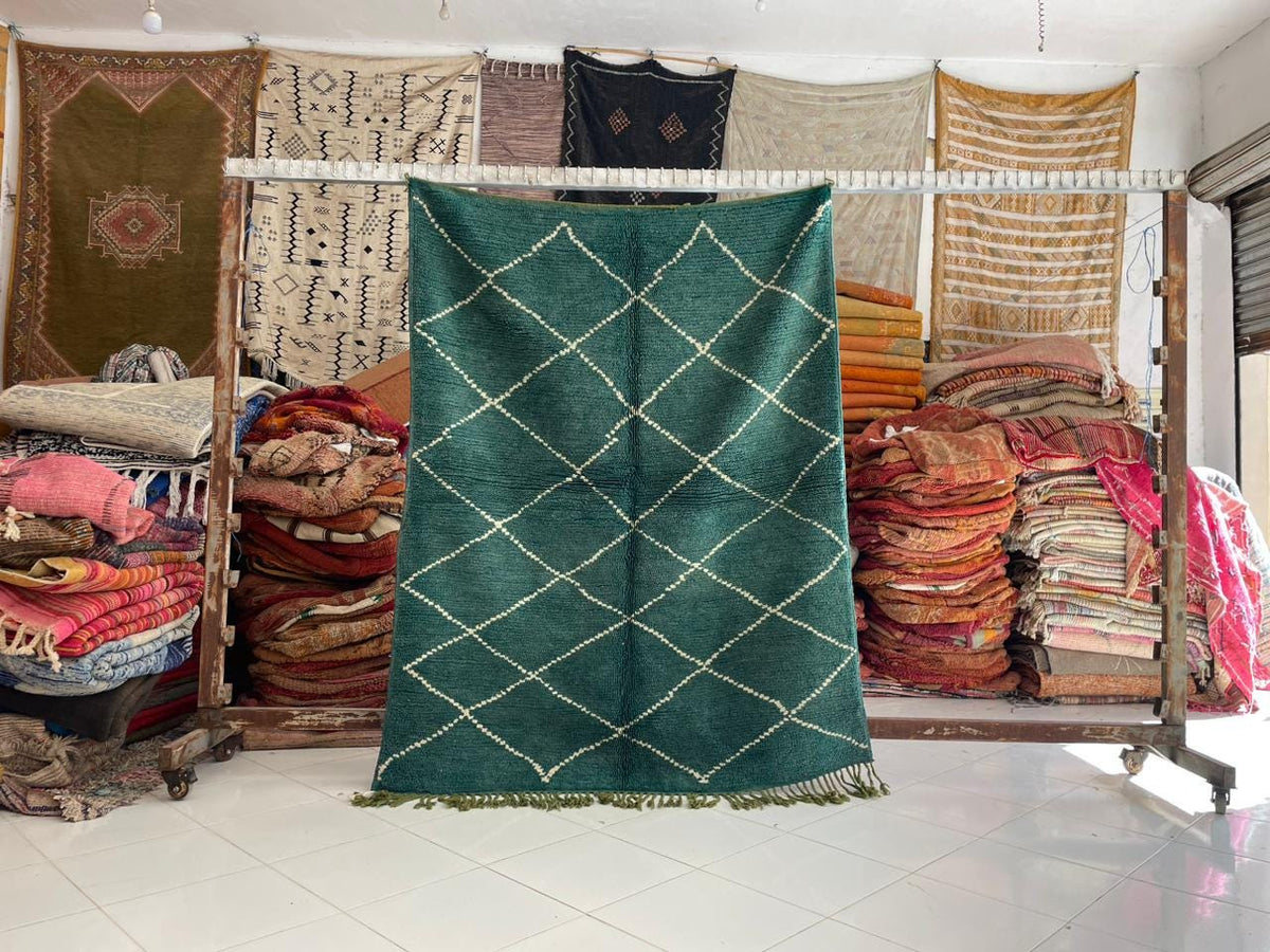 Lifestyle shot of a green wool rug with a geometric pattern displayed against a natural background.
