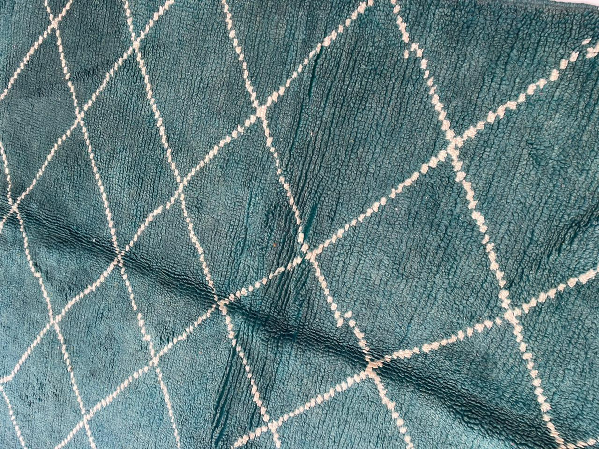 Detail close-up of a green Moroccan rug highlighting the diamond pattern and fringe edges on a white background.