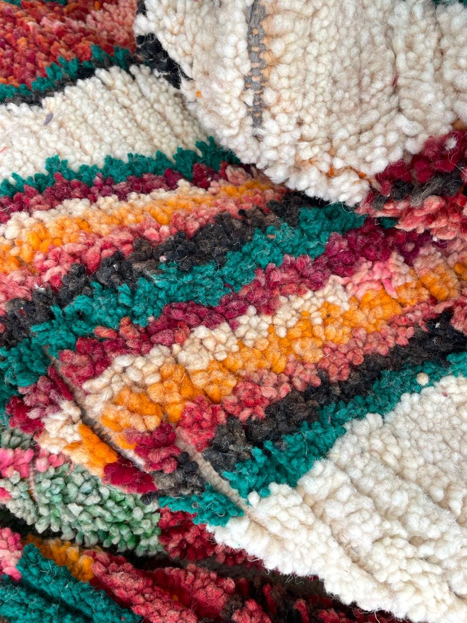 Detail shot of a woven rug showcasing a striped design in red, orange, green, and cream.
