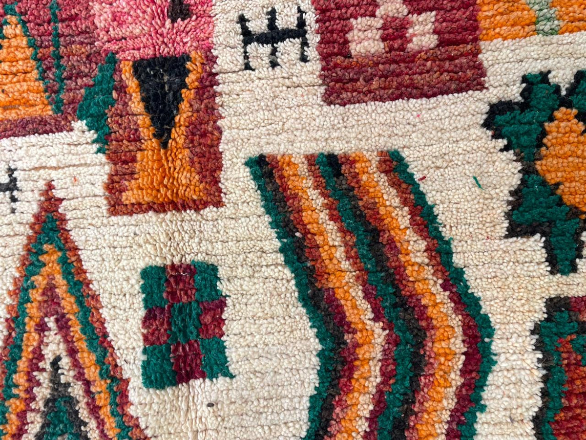 Detail shot of a Moroccan rug highlighting geometric designs in beige, orange, green, and red.