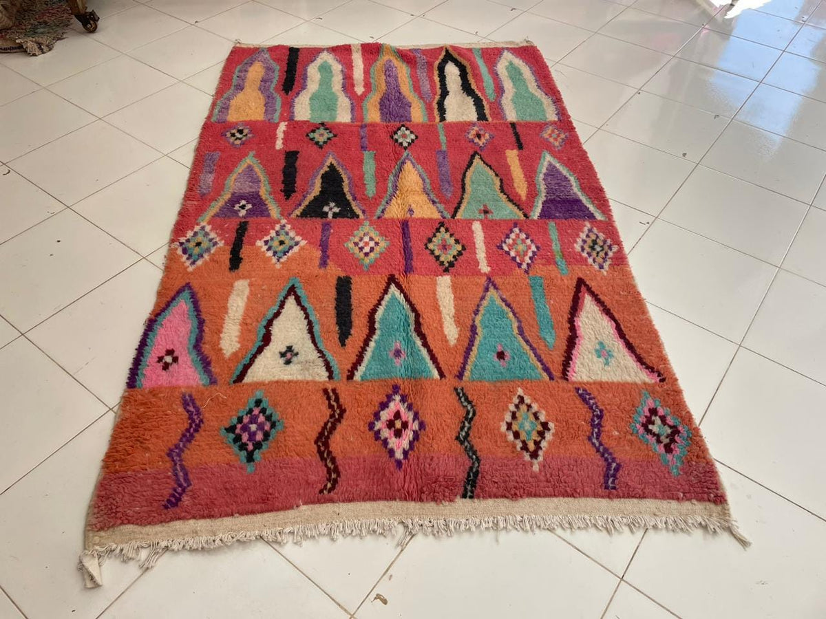 Front view of a vintage Moroccan rug with fringe edges and colorful design in orange, pink, and blue.