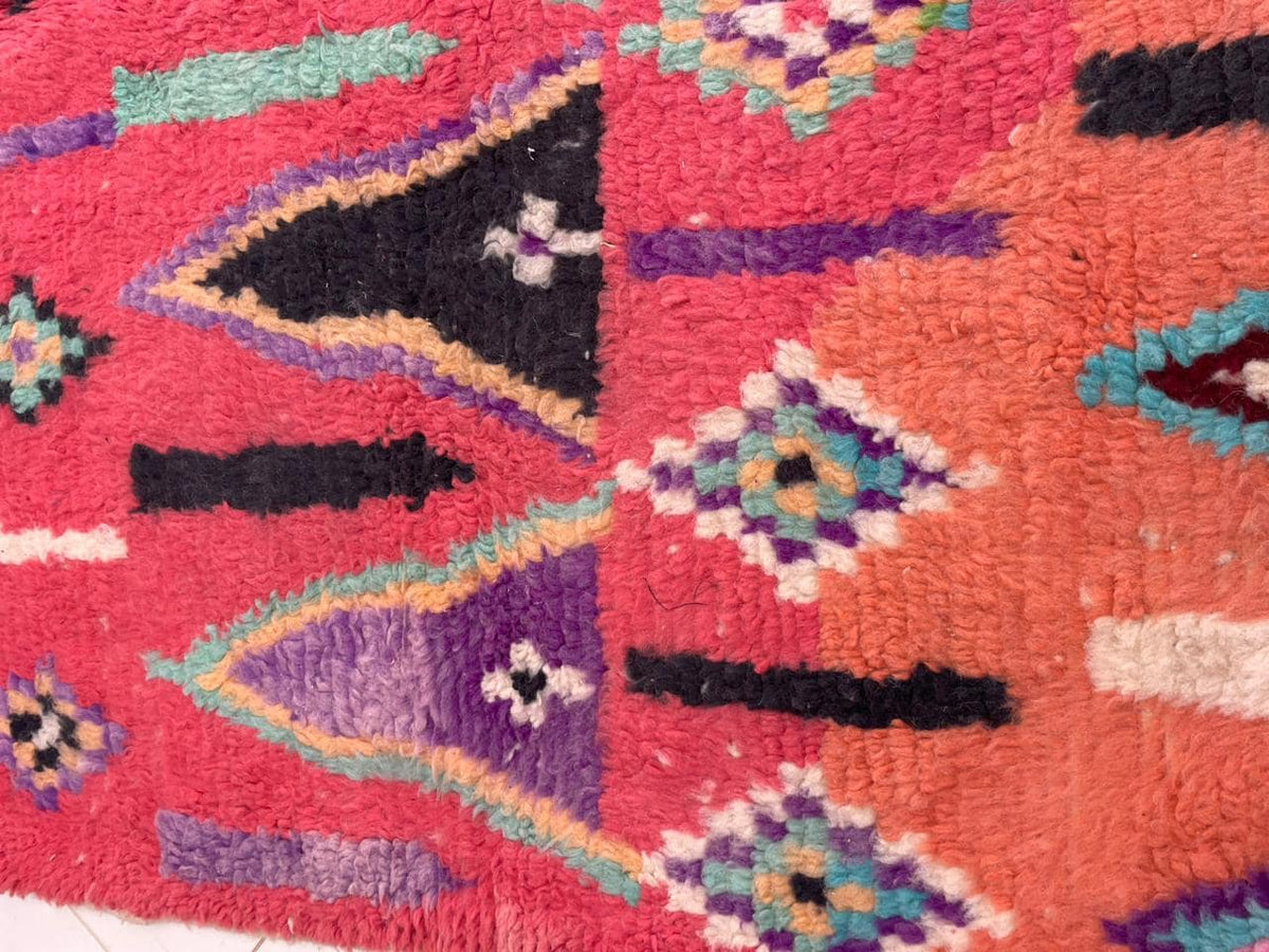 Detail close-up of a vintage Moroccan rug featuring geometric patterns in orange, turquoise, and pink.