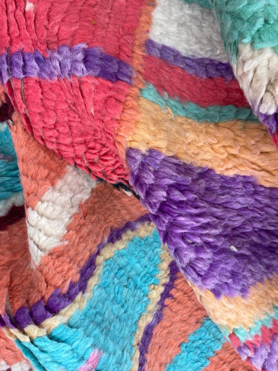 Detail close-up of a vintage Moroccan rug displaying colorful patterns in blue, orange, and purple.
