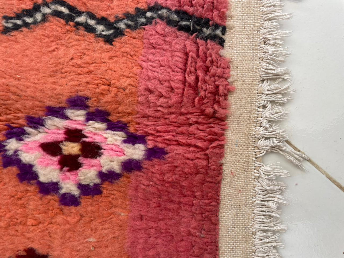 Detail close-up of a vintage Moroccan rug featuring geometric patterns and fringe edges in orange, pink, and black.