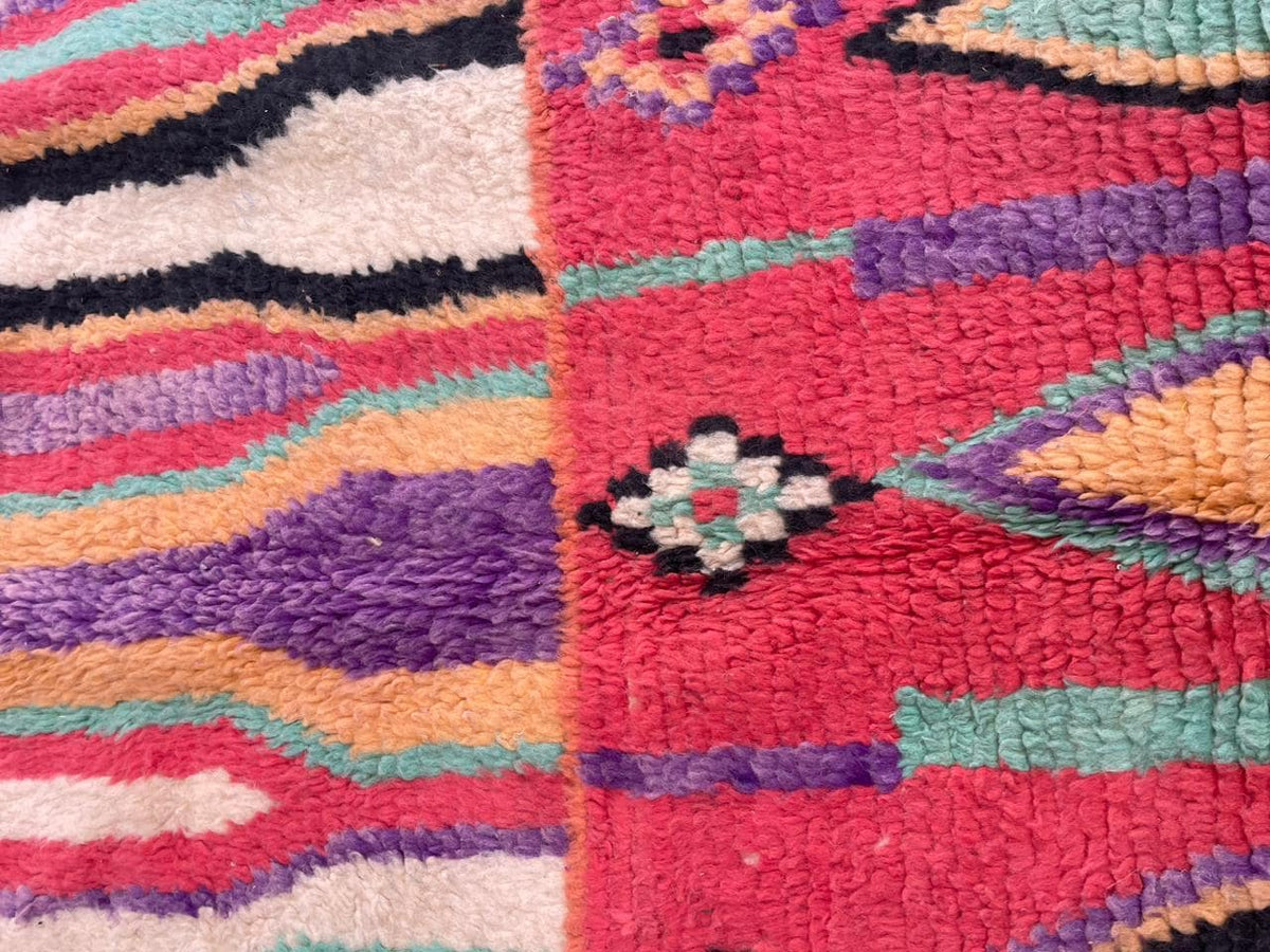 Detail close-up of a vintage Moroccan rug displaying colorful stripes and geometric motifs in red, blue, and purple.